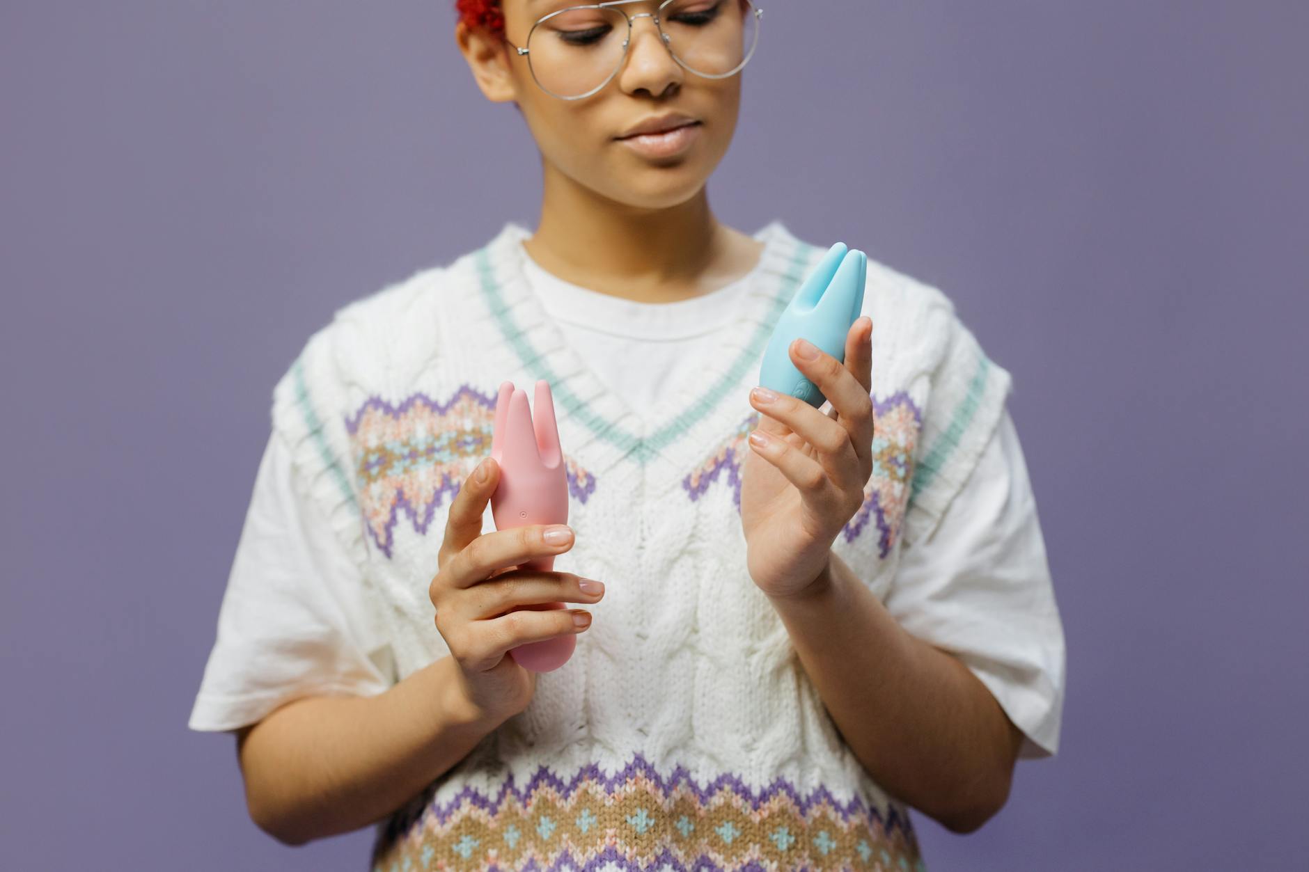 青とピンクのシリコン製バイブレーターを持つ眼鏡をかけた女性が思慮深い表情で立っている